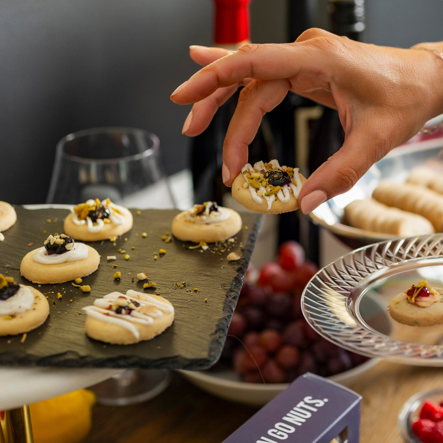 Person serving small appetizers onto a plate with grapes and other snacks in the background