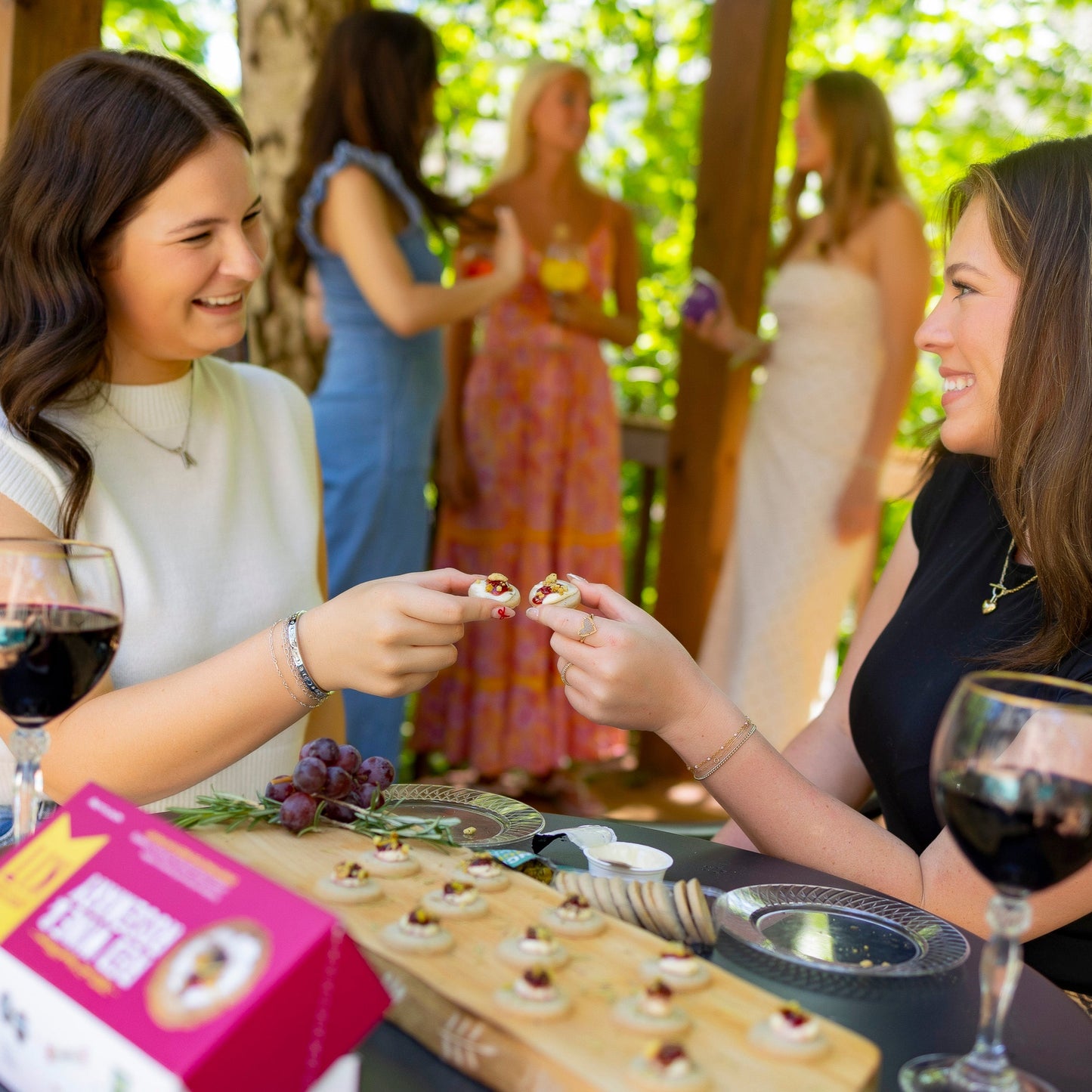 
                  
                    Two women enjoying wine and snacks at an outdoor gathering.
                  
                