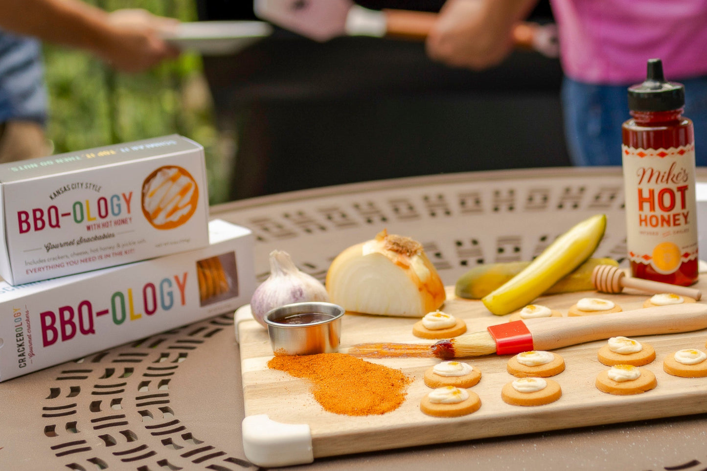 
                  
                    Outdoor setting with people grilling, featuring BBQ-themed products on a table.
                  
                