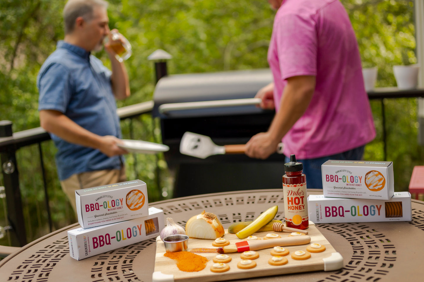 
                  
                    Two men grilling outdoors with BBQ-ology products on a table in the foreground.
                  
                