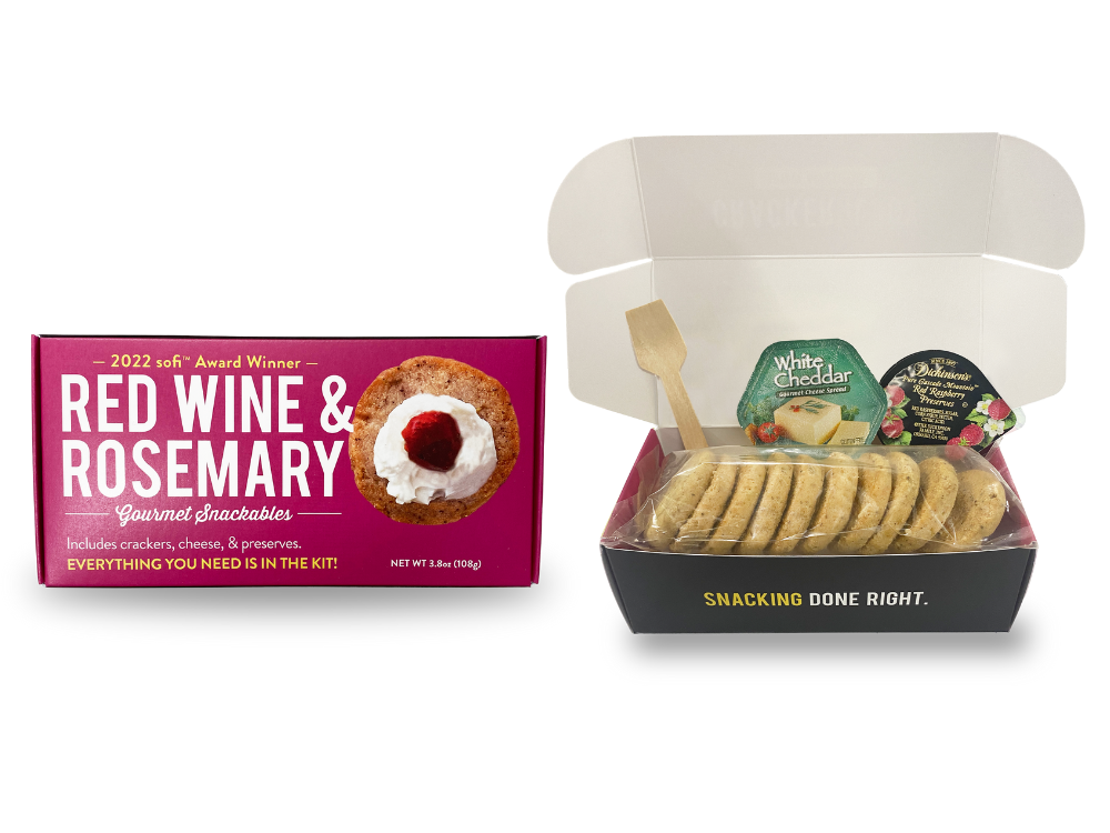 A packaged snackable red wine and rosemary crackerology kit which includes crackers, cheese, and jam.
